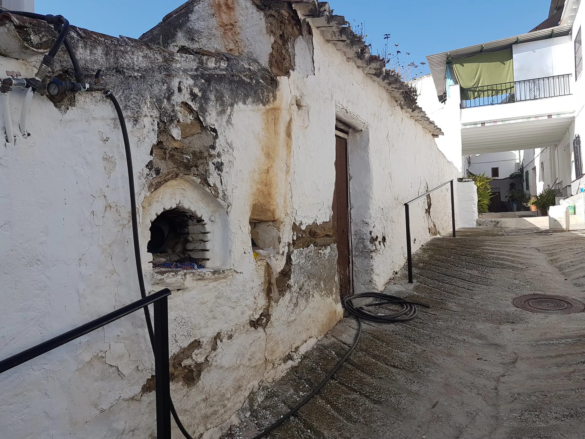 Callejón empedrado entre casas encaladas con un horno de pared y la cal desconchada en Canillas de Aceituno