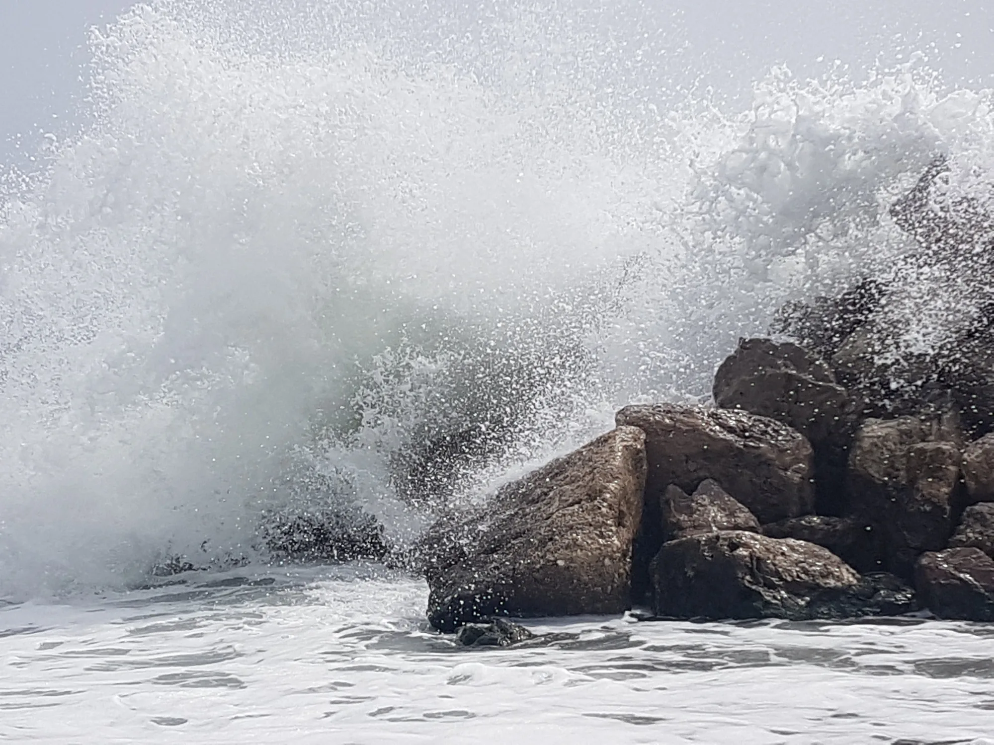 Ola rompiendo contra unas rocas y levantando una gran cortina de espuma en Torre del Mar