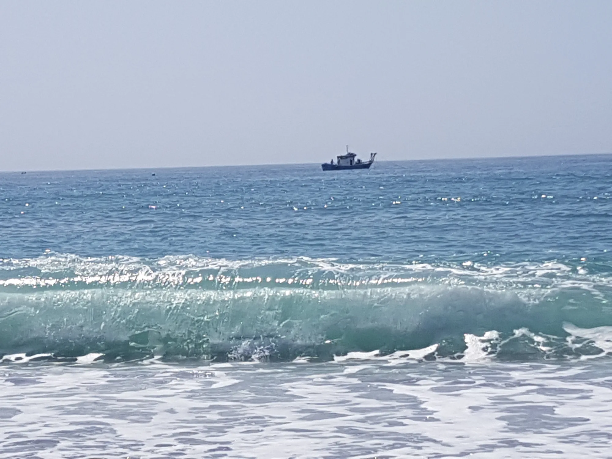 Ola turquesa a punto de romper con un barco pequeño en el horizonte en Chilches