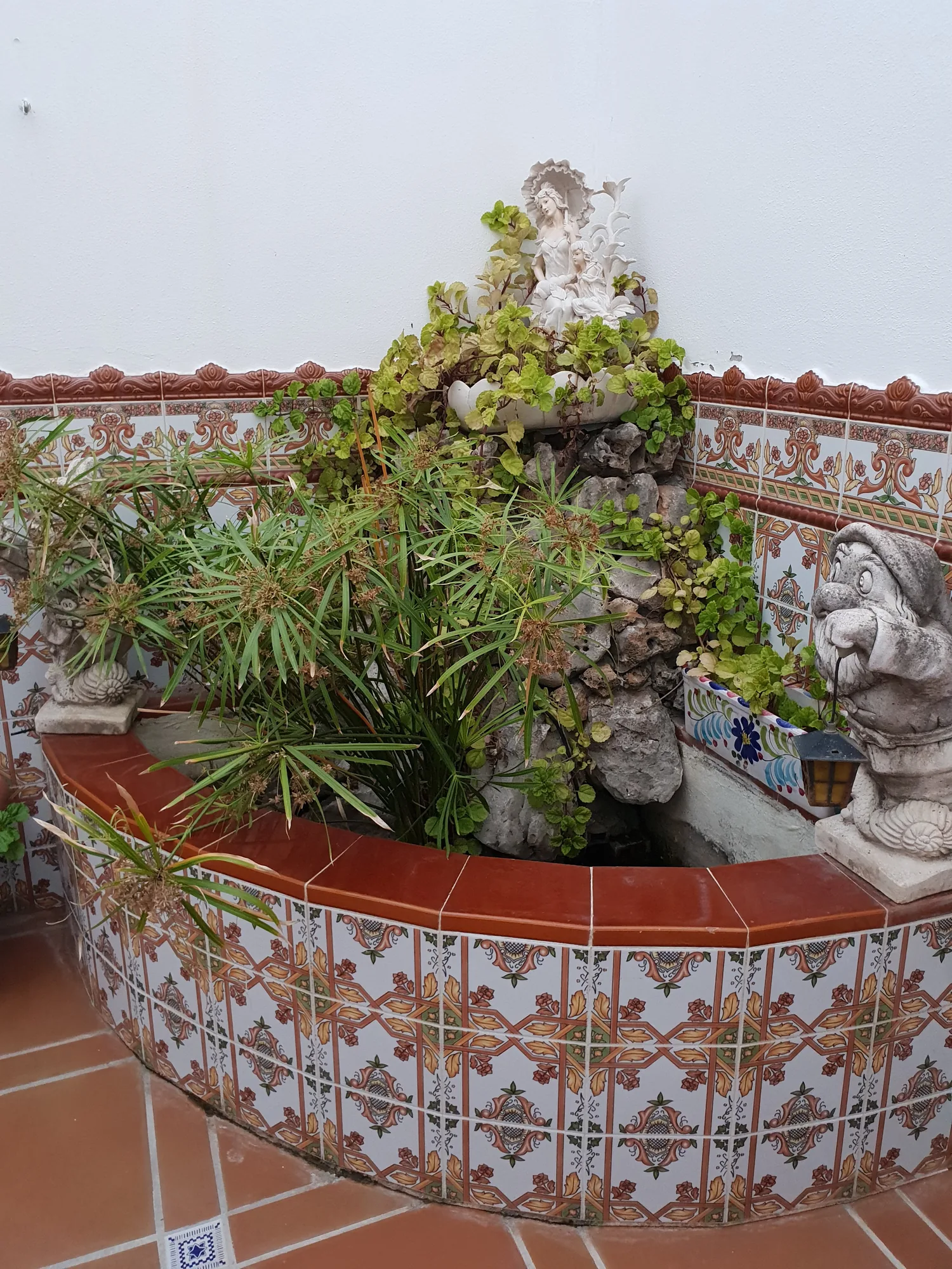 Fuente circular decorada con azulejos y plantas en un patio blanco en Vélez-Málaga