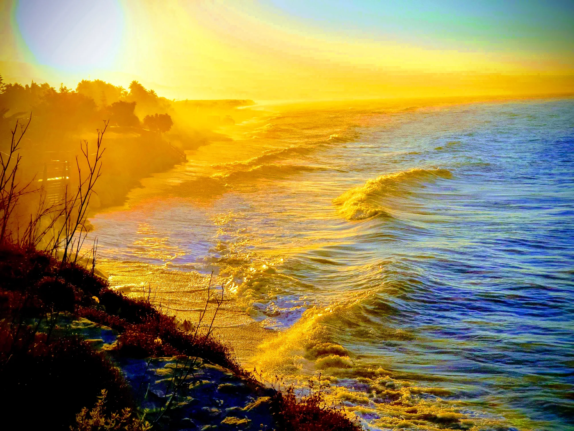 Olas bañadas por una luz dorada intensa al amanecer junto a una ladera con vegetación en Almayate