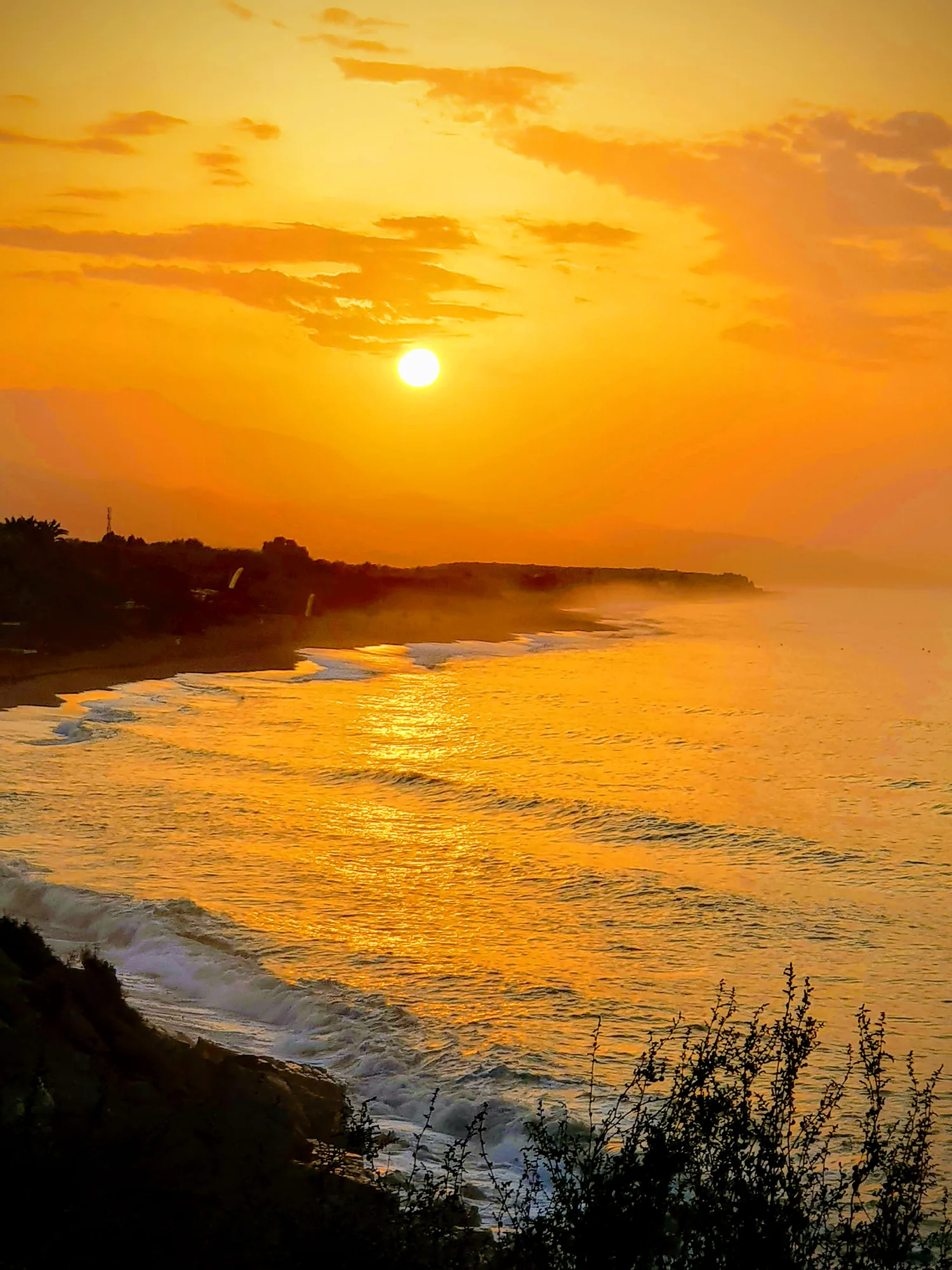 Sol naranja sobre una cala con la costa envuelta en bruma y el mar iluminado en Almayate