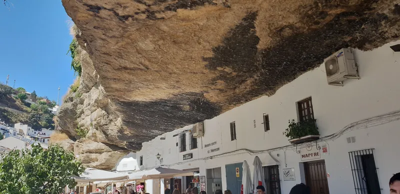 Calle con casas blancas construidas bajo un gran saliente de roca