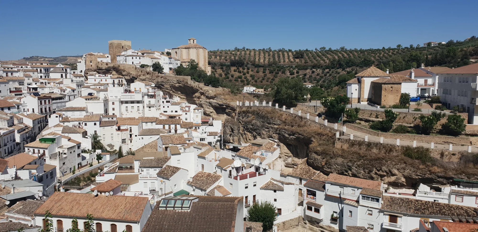 Vista sobre tejados de un pueblo de casas blancas rodeado de olivar en Setenil de las Bodegas