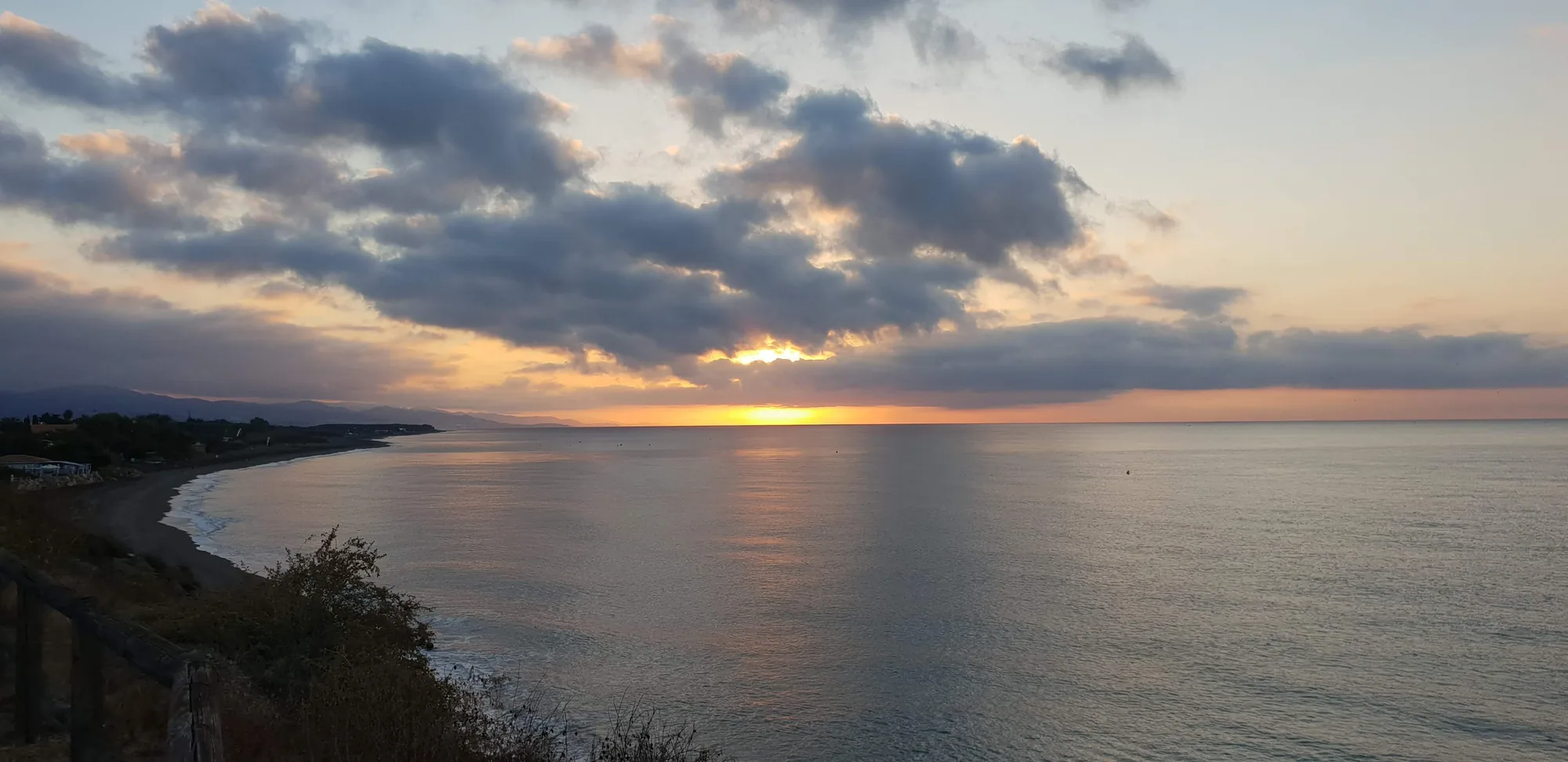 Amplia vista de la costa al amanecer con nubes iluminadas y el mar en calma en Valle-Niza