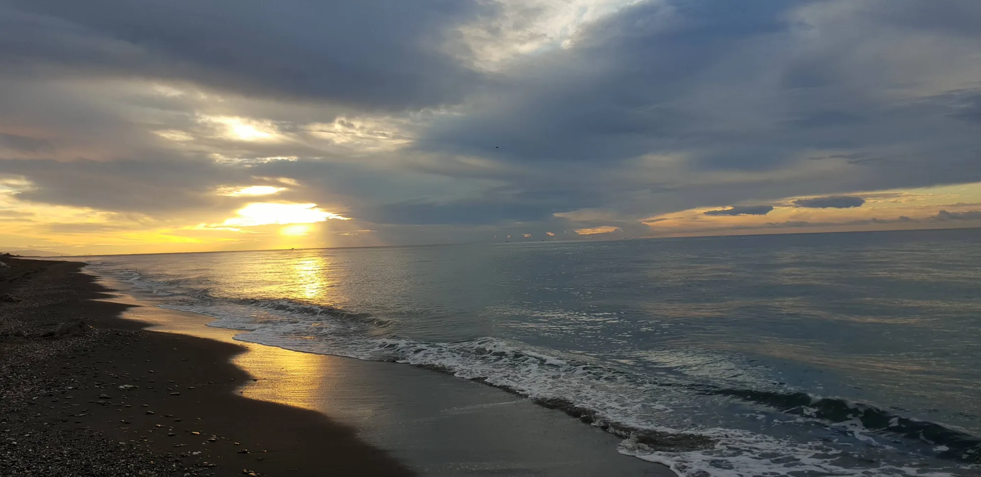 Cielo cargado de nubes con rayos de sol sobre una playa y el mar en Almayate