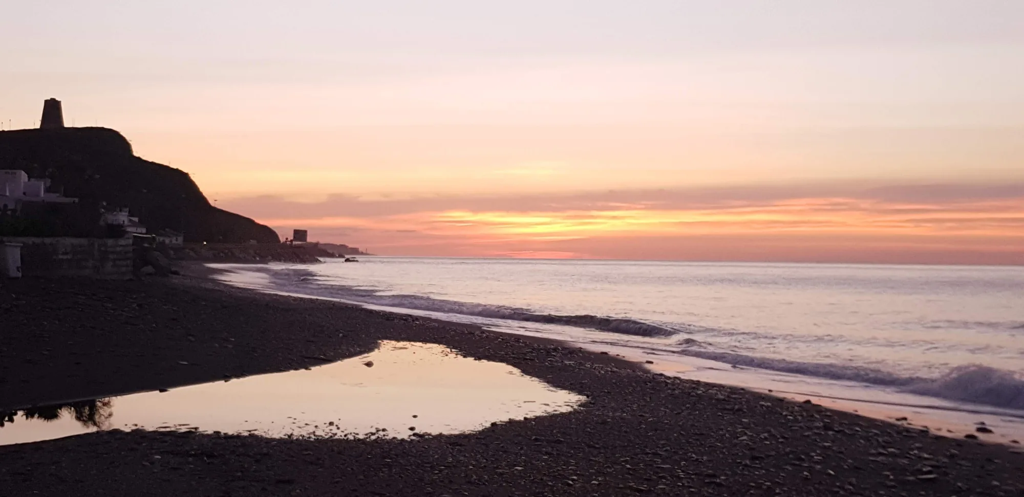 Playa de cantos con una charca que refleja el cielo rosado del amanecer en Lagos
