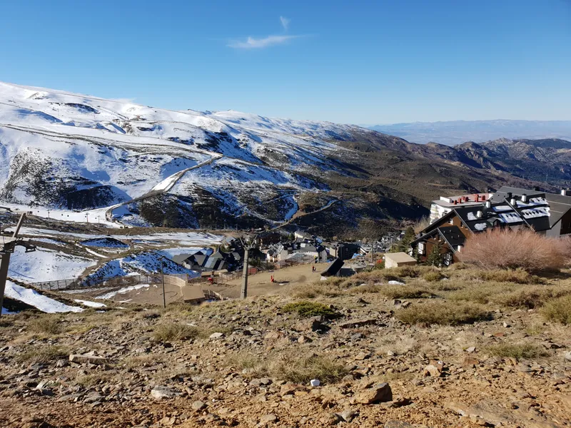 Montañas con nieve bajo un cielo azul y un conjunto de edificios en la ladera