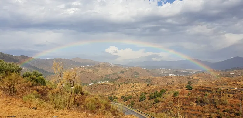 Arcoíris sobre montañas secas con pueblos blancos y una carretera