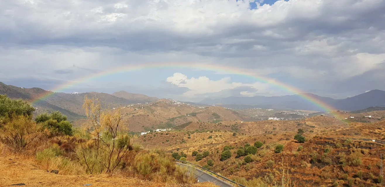Arcoíris sobre montañas secas con pueblos blancos y una carretera en Canillas de Aceituno