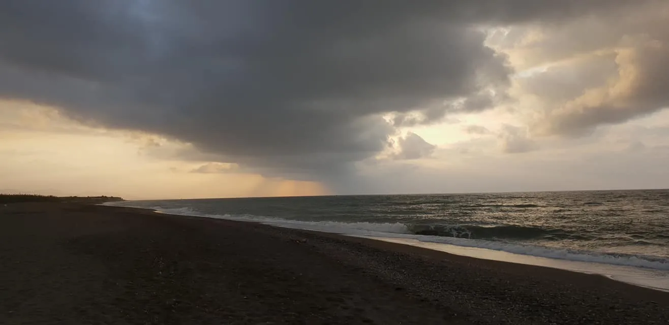 Nubes de tormenta sobre una playa con una cortina de lluvia en el horizonte en Valle-Niza