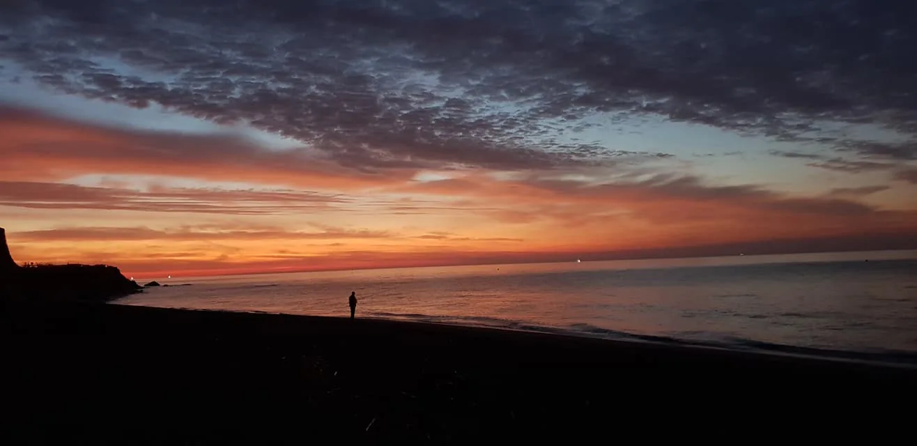 Una persona pequeña en la orilla bajo un cielo de nubes rojizas al amanecer en Valle-Niza