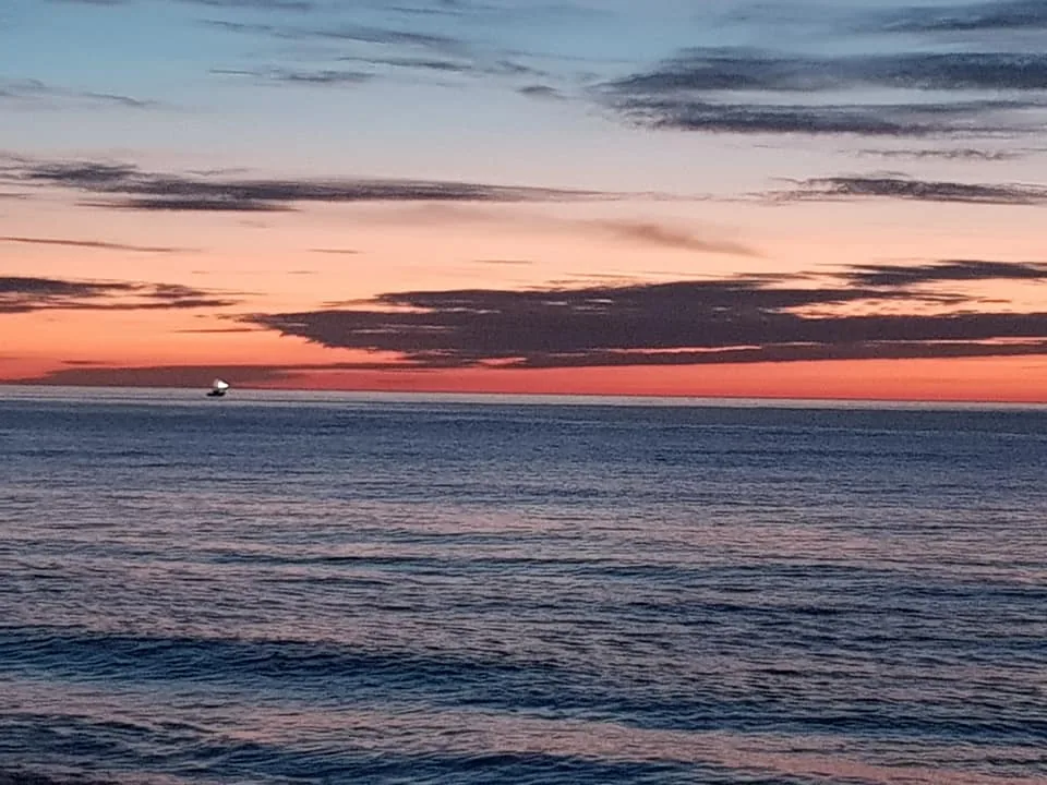 Cielo rosa y azul oscuro sobre el mar con una pequeña barca en el horizonte en Valle-Niza