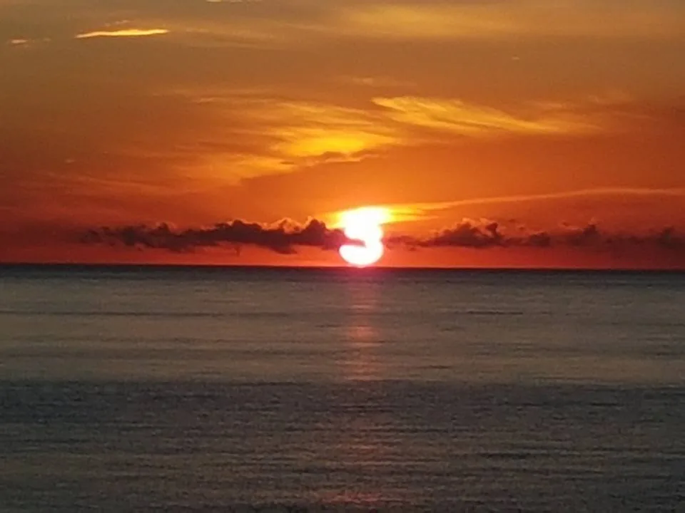 Sol rojo sobre el horizonte con el cielo naranja y nubes alargadas en Almayate