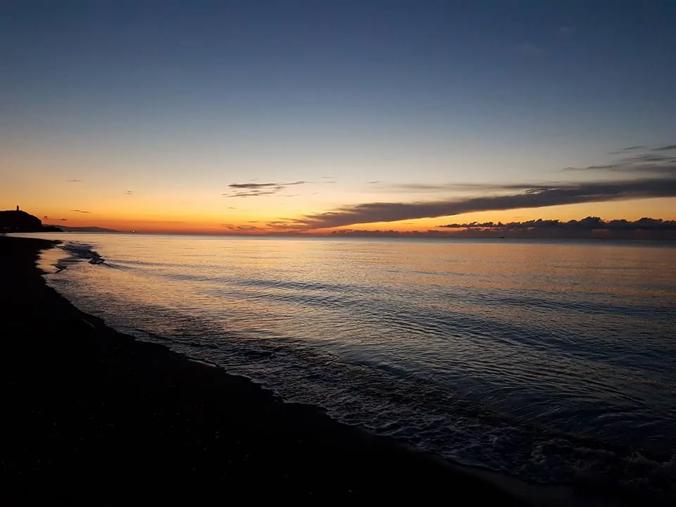 Playa oscura al anochecer con un último resplandor naranja en el horizonte en Almayate