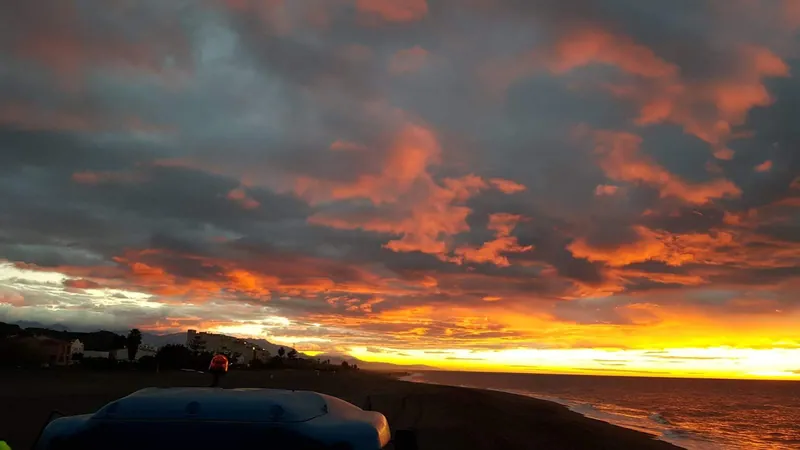 Nubes naranjas y oscuras sobre una playa al atardecer con el último sol en el horizonte