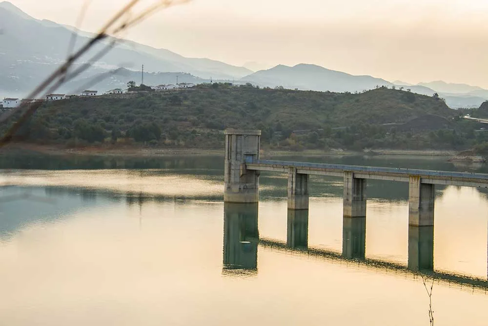 Torre de toma de agua y pasarela sobre un embalse con montañas al fondo en La Viñuela
