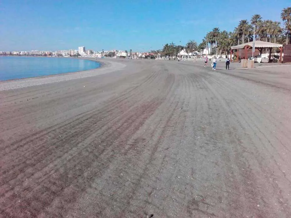 Amplia playa de arena con paseantes y palmeras al fondo en Torre del Mar