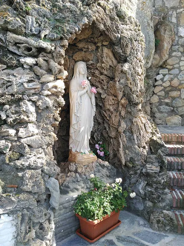 Imagen de la Virgen en una hornacina de piedra con flores